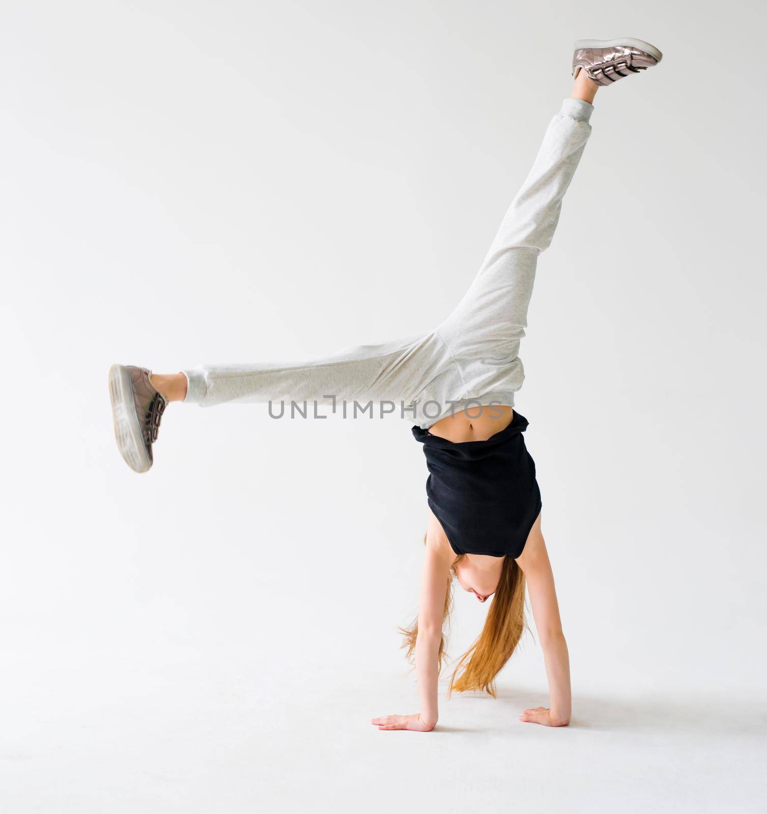 Attractive flexible teenage girl doing handstand on light background