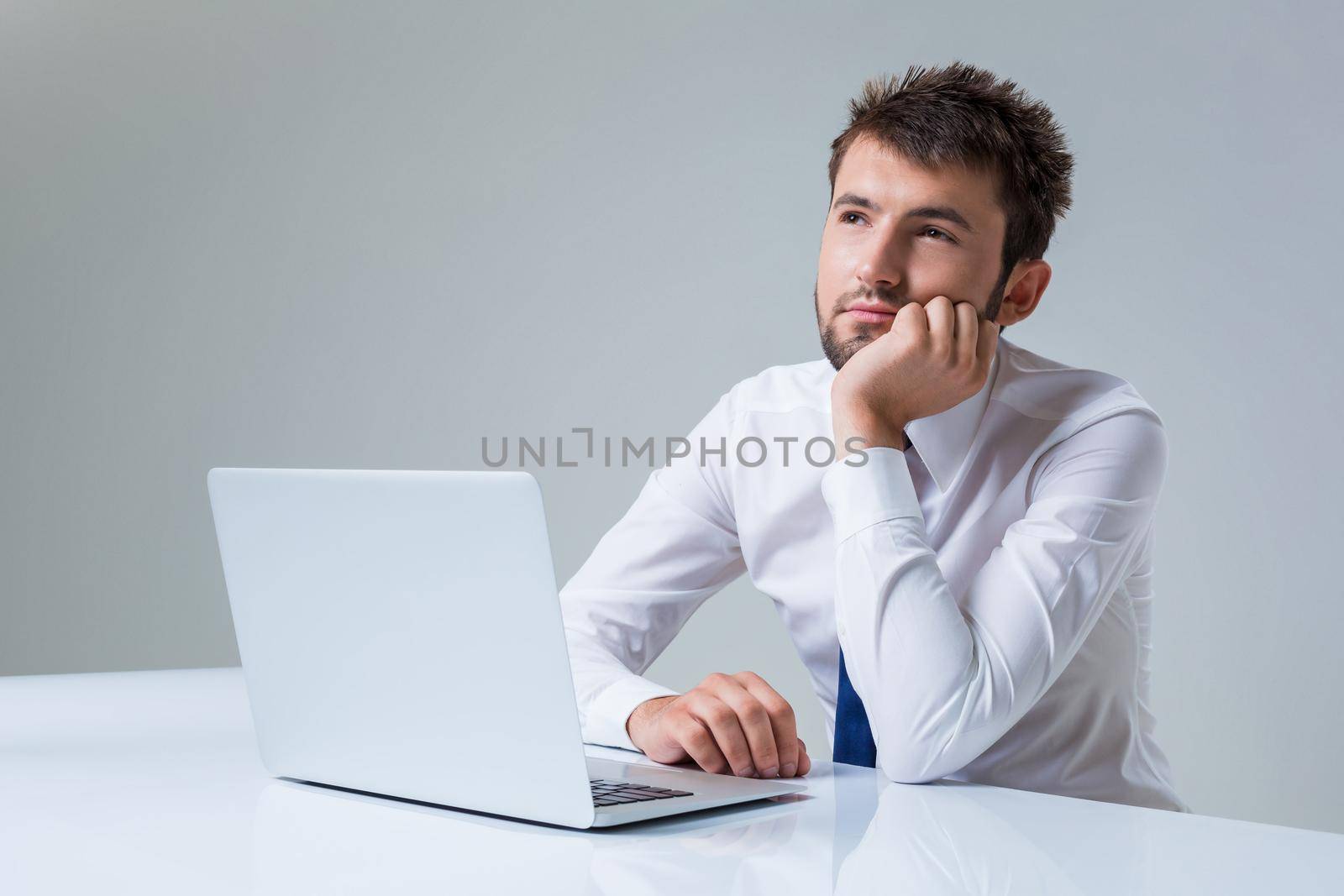 young man thinking uses a laptop computer while sitting at a table. Office clothing