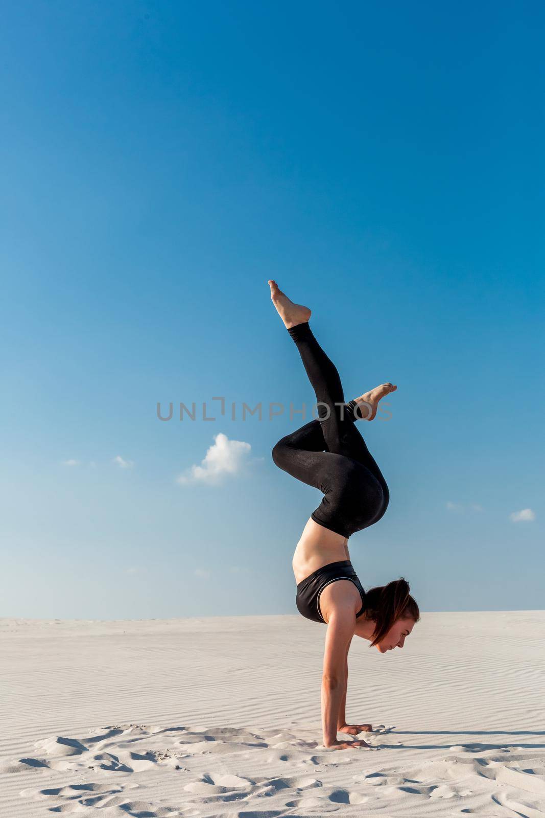 Young woman practicing handstand on beach with white sand and bright blue sky by nazarovsergey