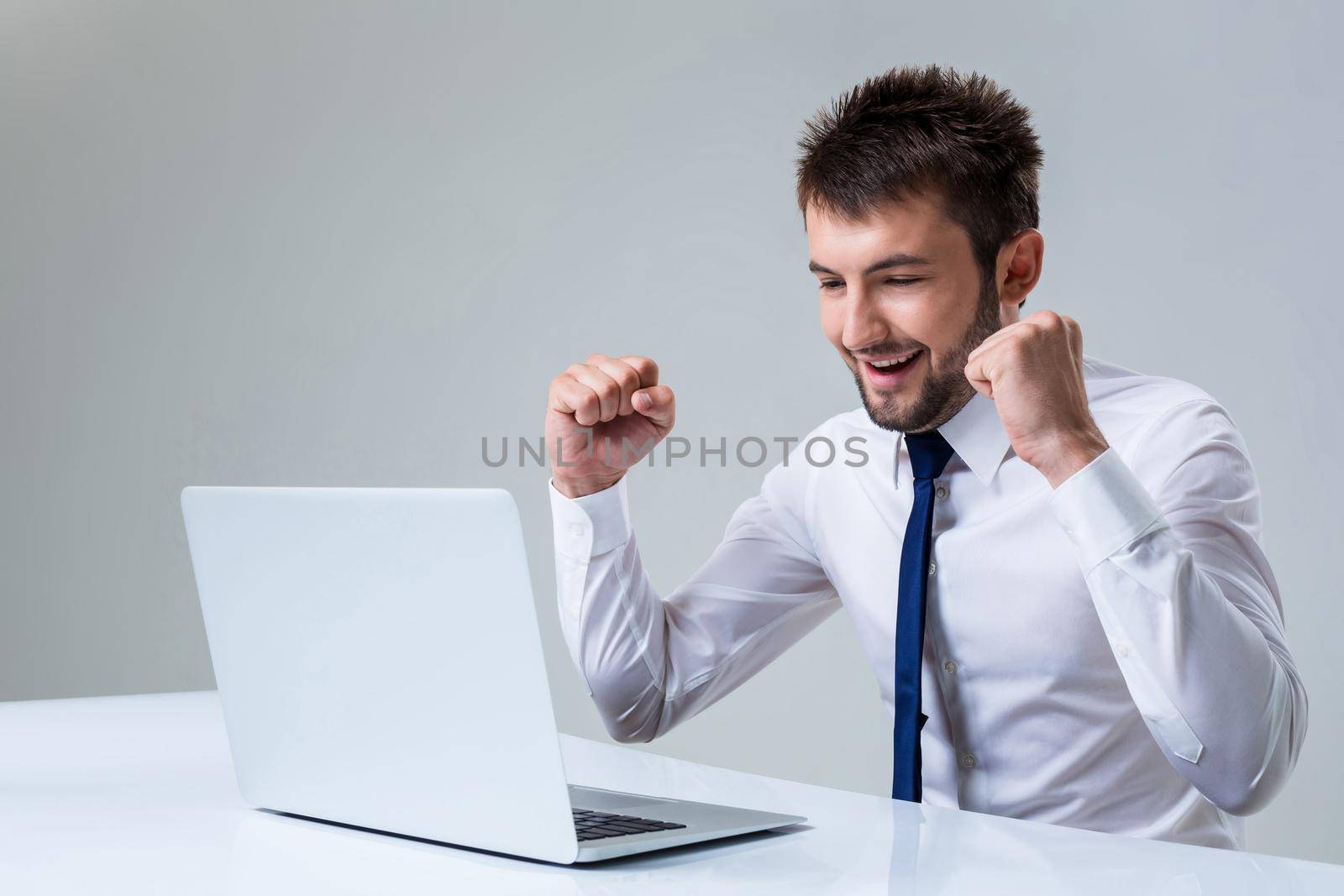 young man smiling and enjoys uses a laptop computer while sitting at a table. Office clothing