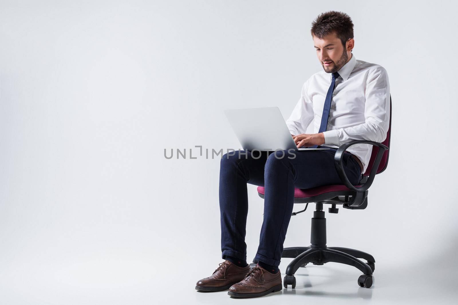 emotional young guy in office clothes working on a laptop computer and sitting on a chair