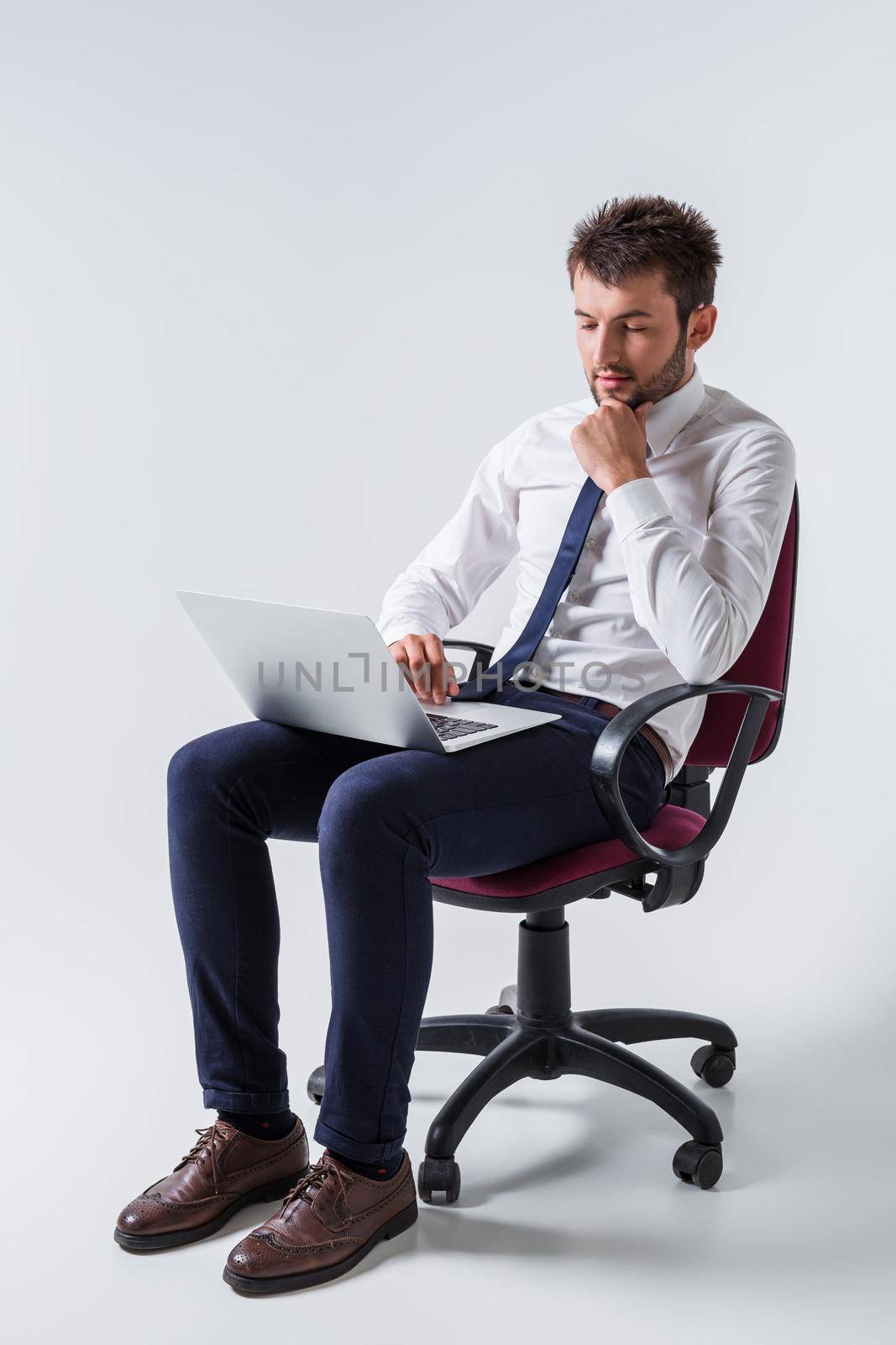 emotional young guy in office clothes working on a laptop computer and sitting on a chair