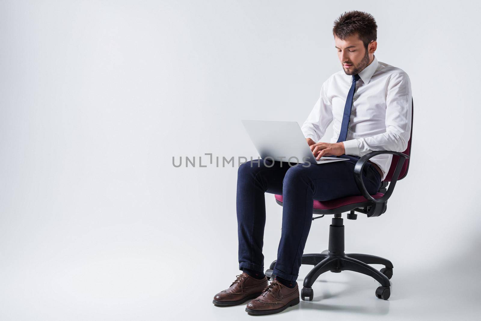 emotional young guy in office clothes working on a laptop computer and sitting on a chair