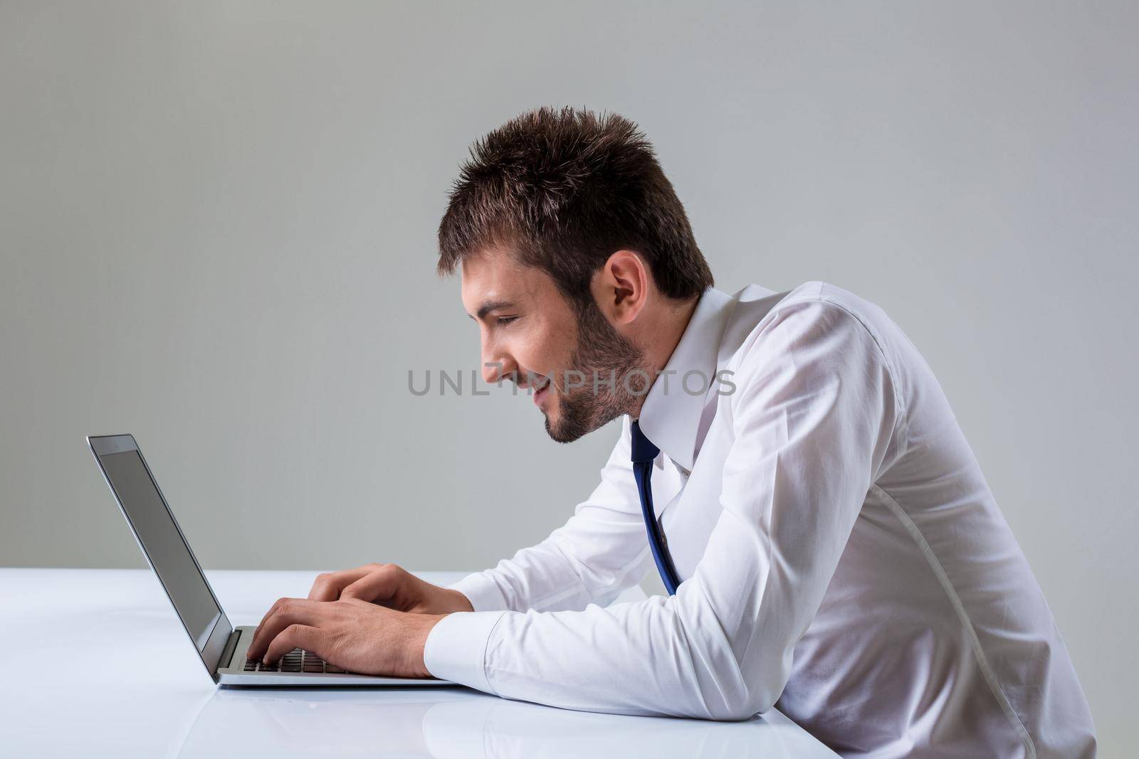 nerd young male smiling and typing on laptop. It uses a computer while sitting at a table. Office clothing