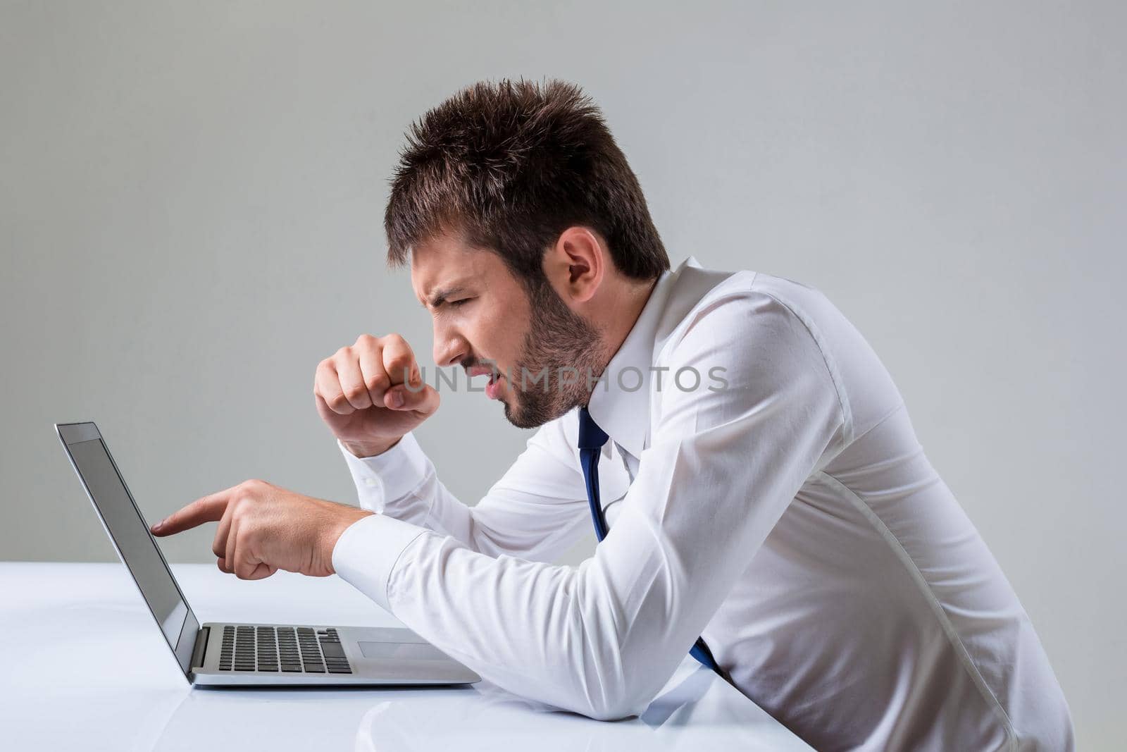 the young man is nervous and poke a finger. It uses a computer while sitting at a table. Office clothing