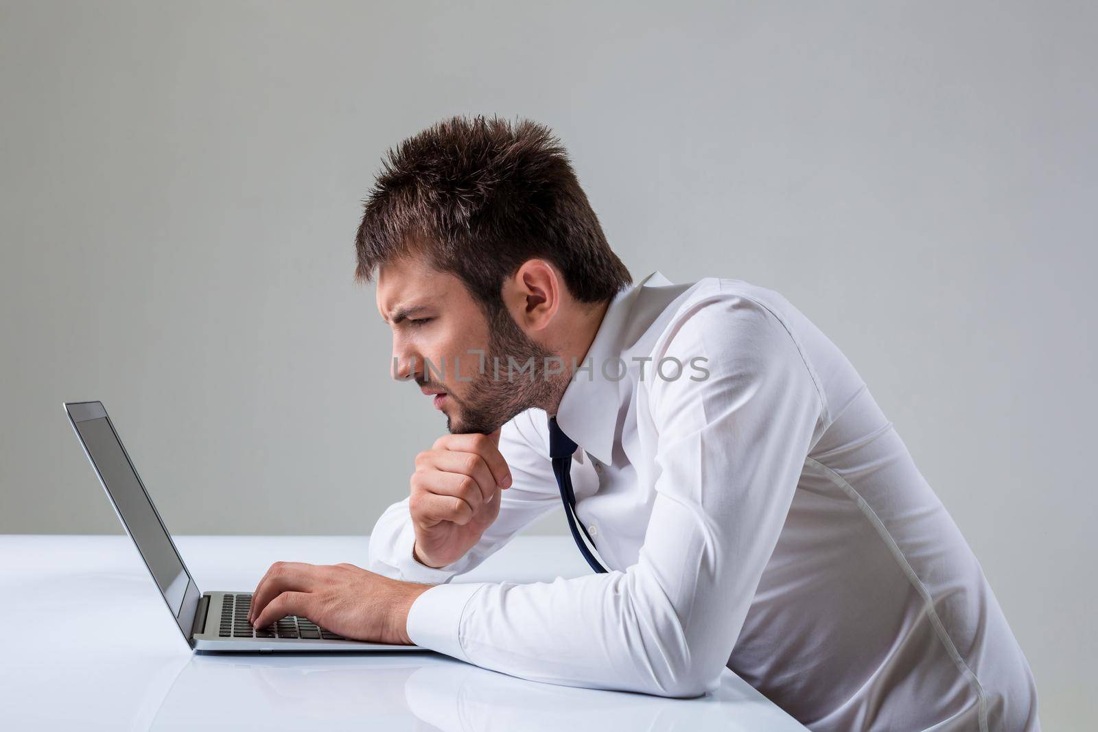 the young man stares at a laptop. It uses a computer while sitting at a table. Office clothing