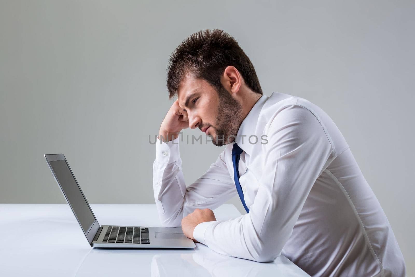 tired young man looking at laptop. It uses a computer while sitting at a table. Office clothing