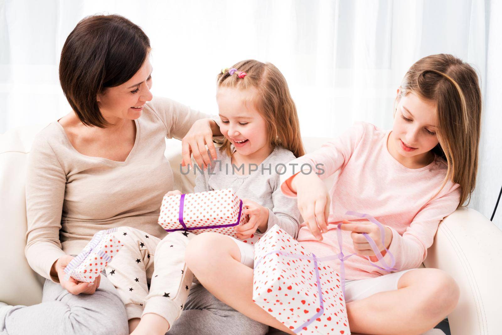 Cheerful mom and her beautiful daughters exchanging gifts Happy birthday, Happy Woman's day, Happy Mother's day, Christmas gifts. Mom and daughters unwrapping gifts