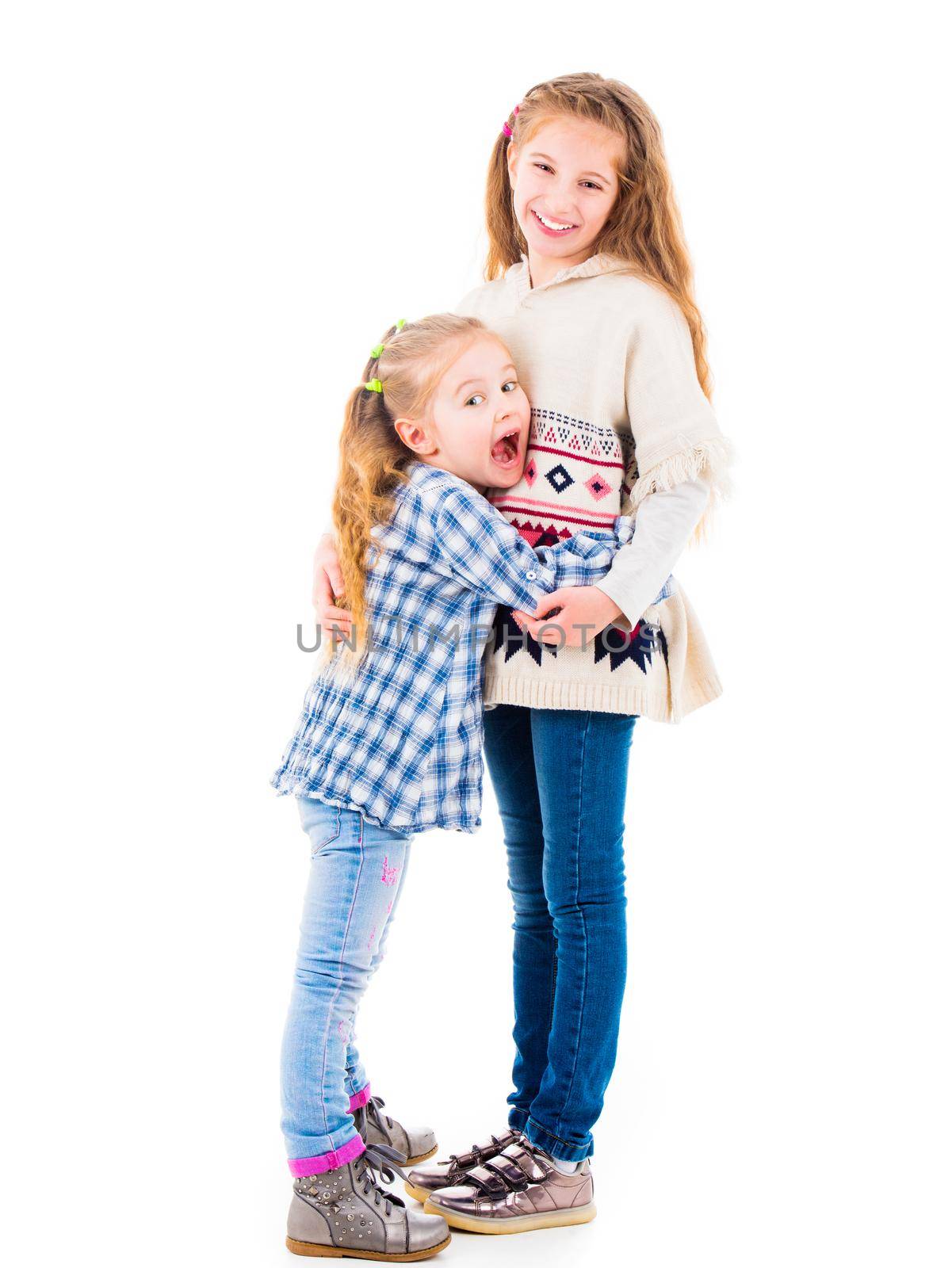 Two little girls sisters in casual clothes posing and hugging each other, isolated on white background