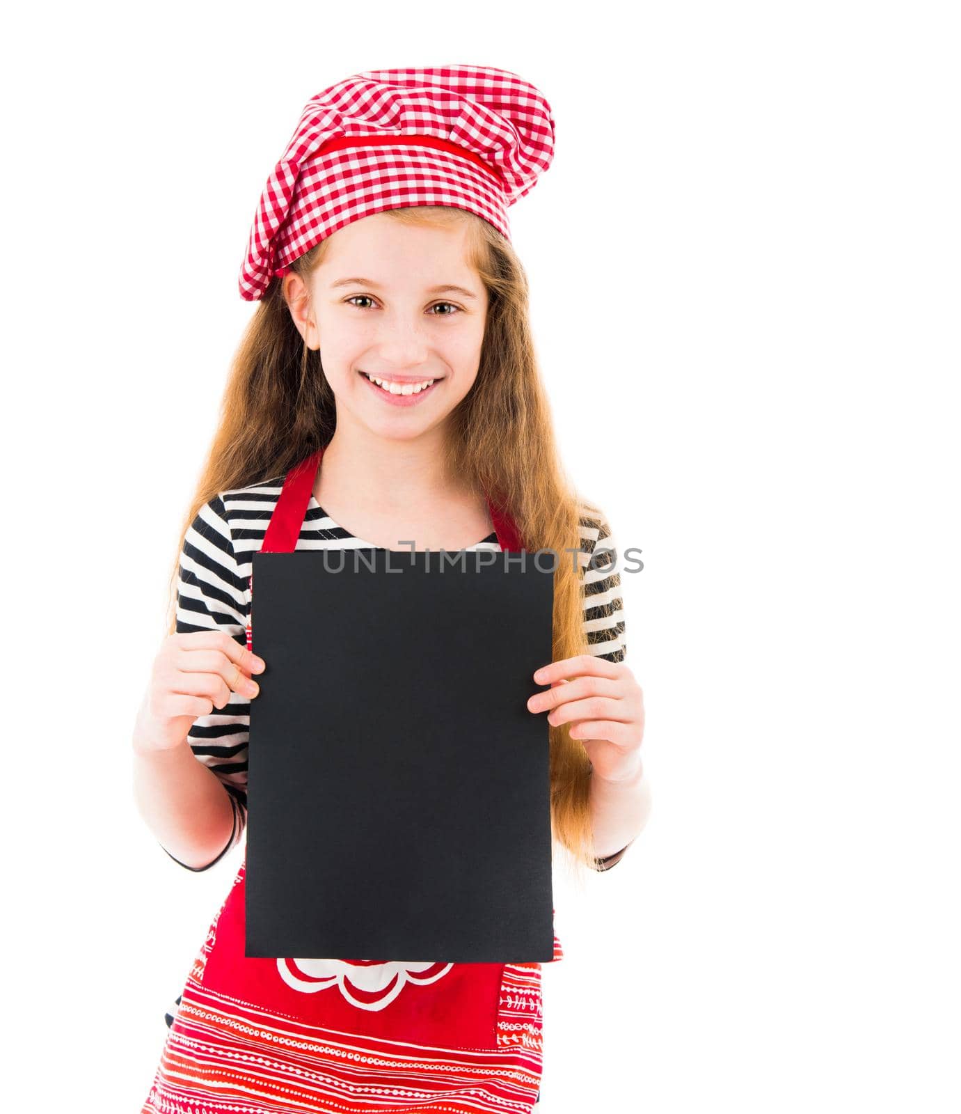 Young little girl in red chef uniform holds vertical blank black sheet of paper and smiles isolated on white background. Copyspace, space for your text, recipe, advertising, menu