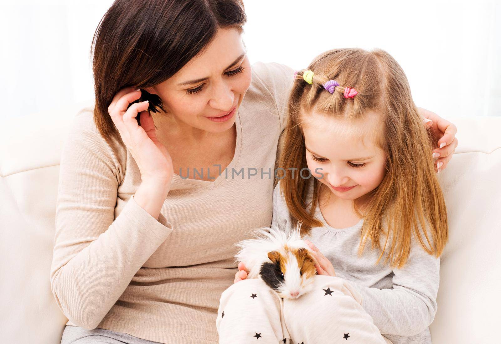 Mom and little daughter playing with guinea pig at home