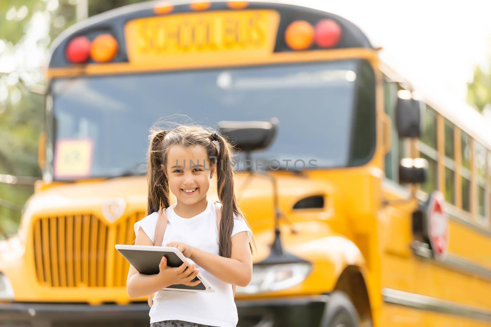 Cute girl with a backpack standing near bus going to school posing to camera pensive close-up by Andelov13