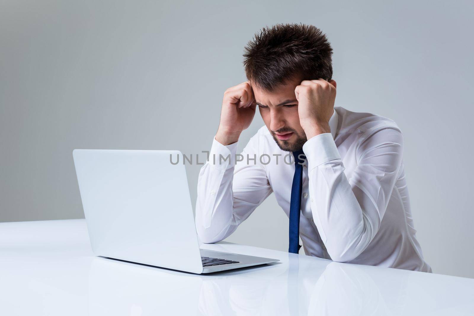 young man frustrated using laptop computer sitting at the table. Office clothing