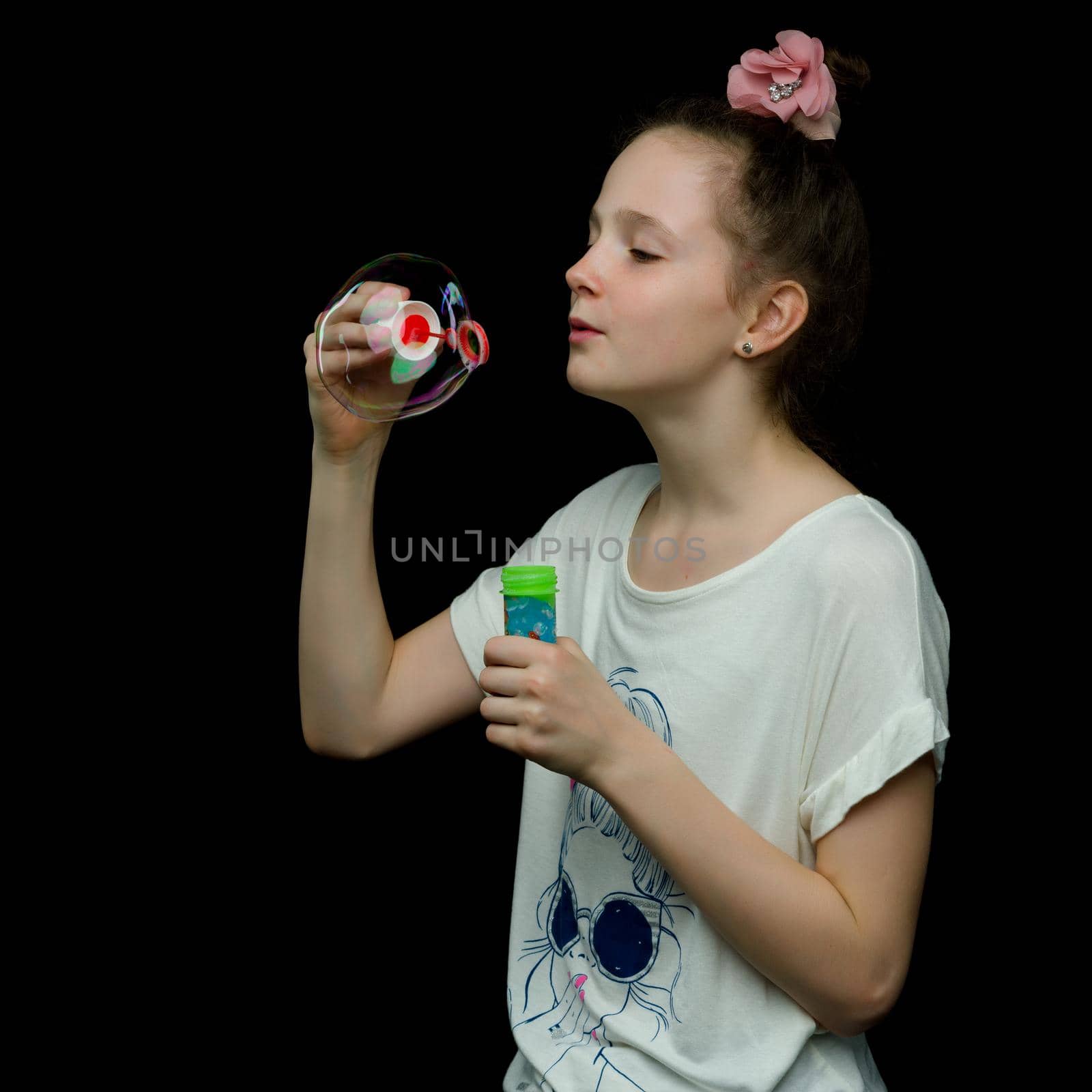 Cute little girl blows soap bubbles. On black background