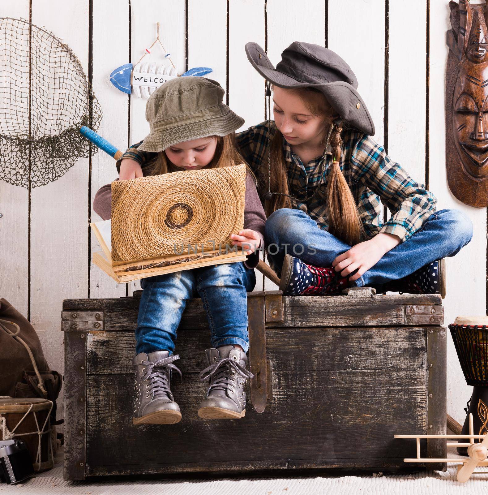two cute little girls in cowboy hats sitting on wooden chest and watching album