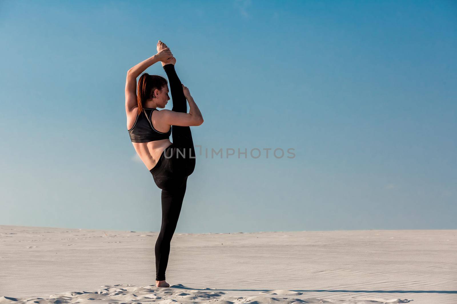 Young slim woman do gymnastic exercise at white sand beach under blue sky. Young gymnast on seashore