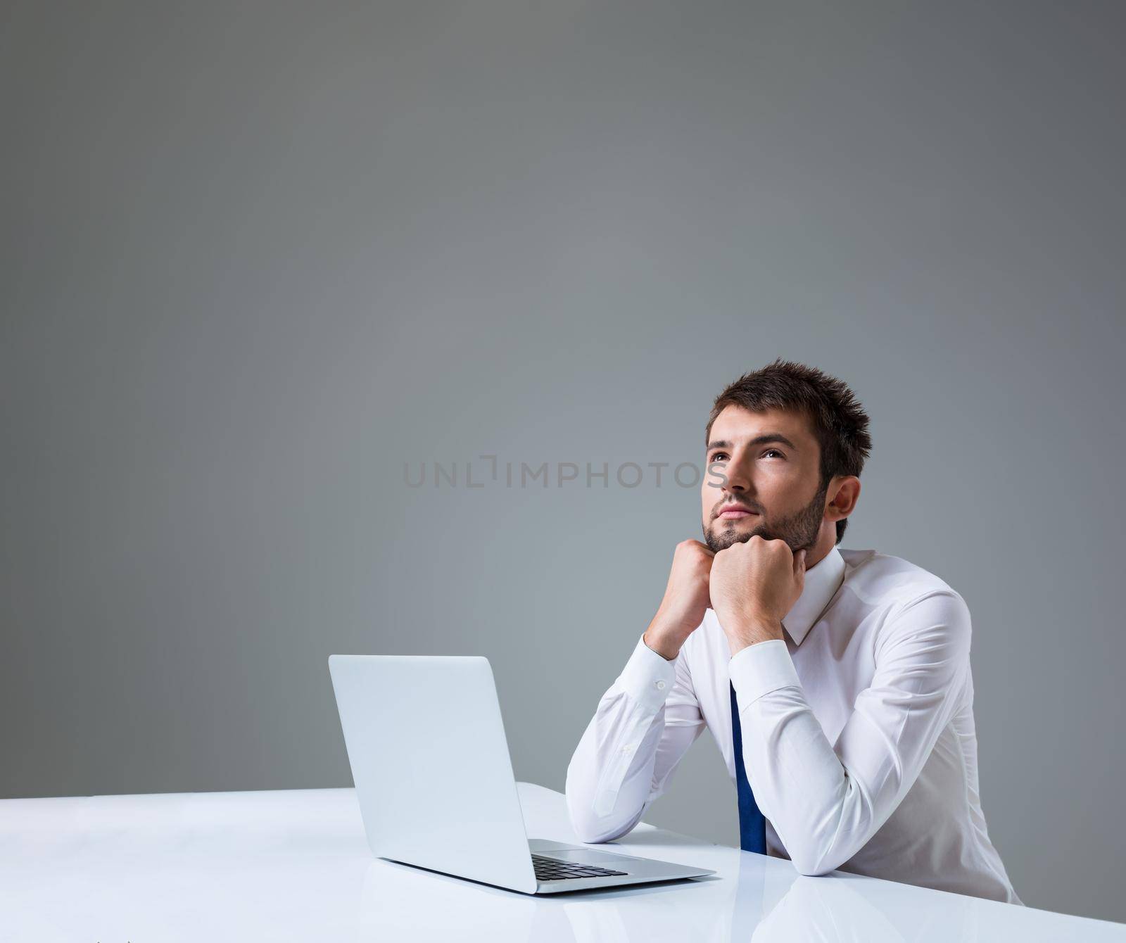 young man thinking uses a laptop computer while sitting at a table. Office clothing. copyspace