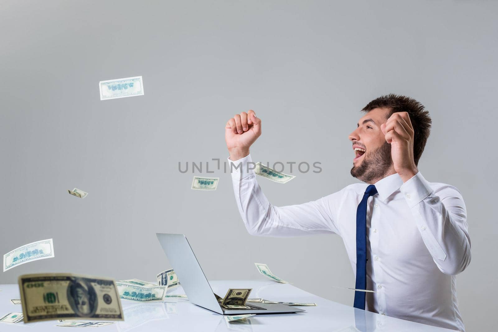 the young man behind the laptop. It uses a computer while sitting at a table. enjoys hands up. Office clothing. the top falling money, dollars