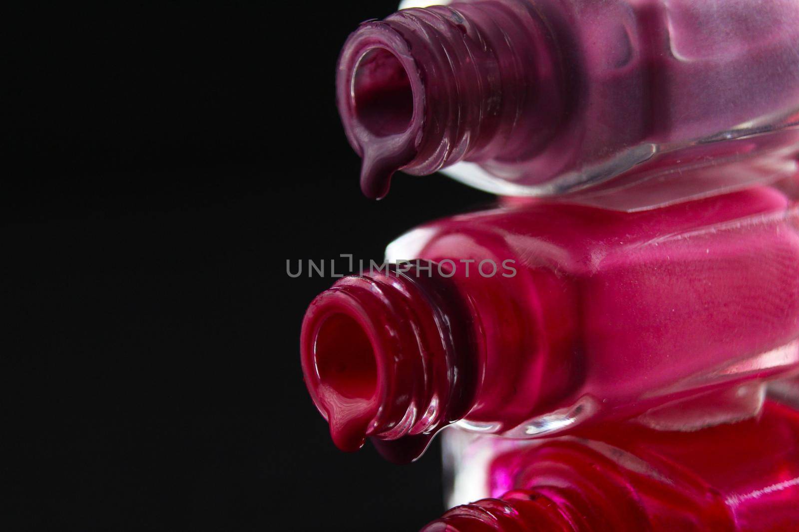 Beauty background saver nail polish is poured out of cans of vials of purple red burgundy pink close-up view from the side.