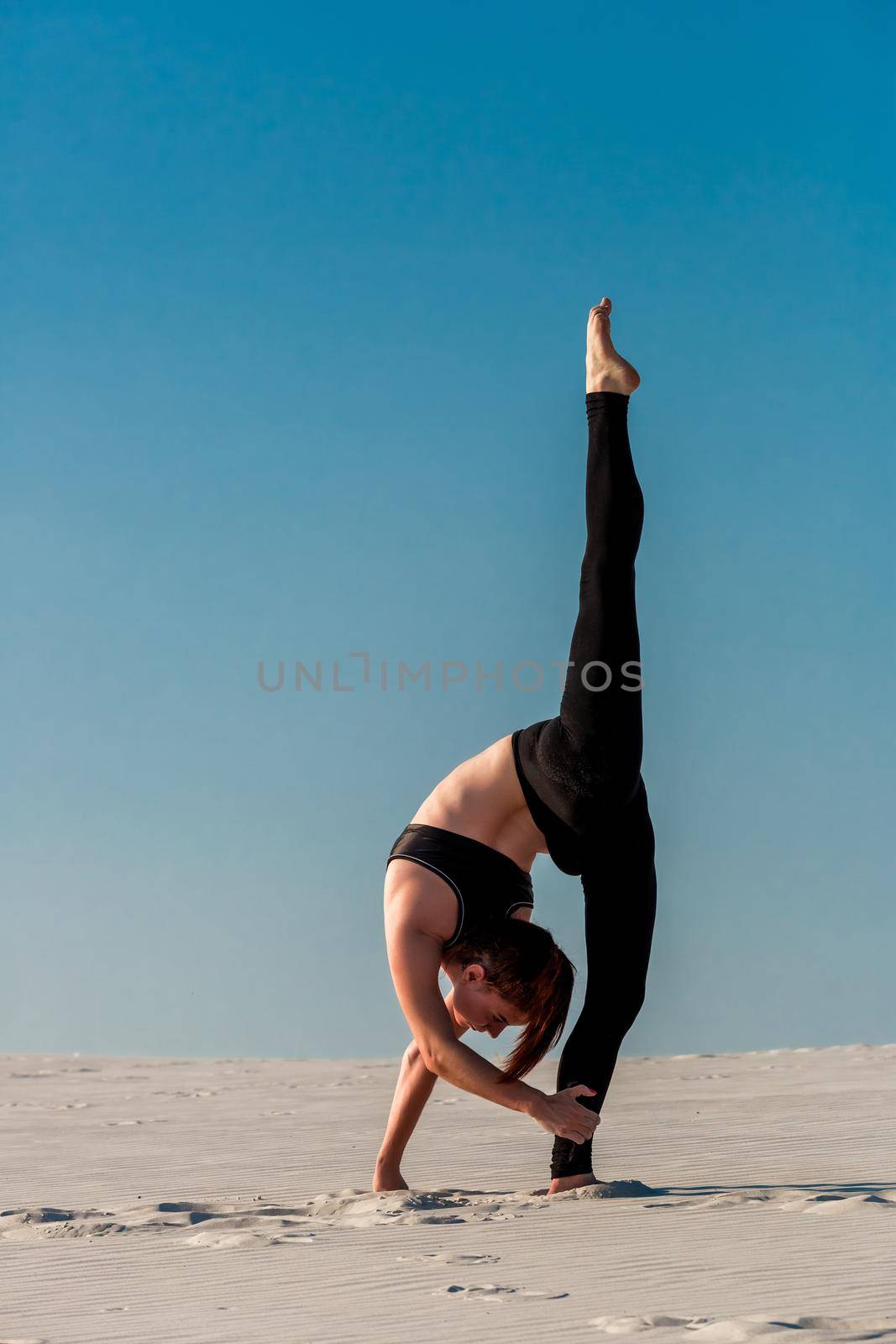 Young slim woman do gymnastic exercise at white sand beach under blue sky. Young gymnast on seashore