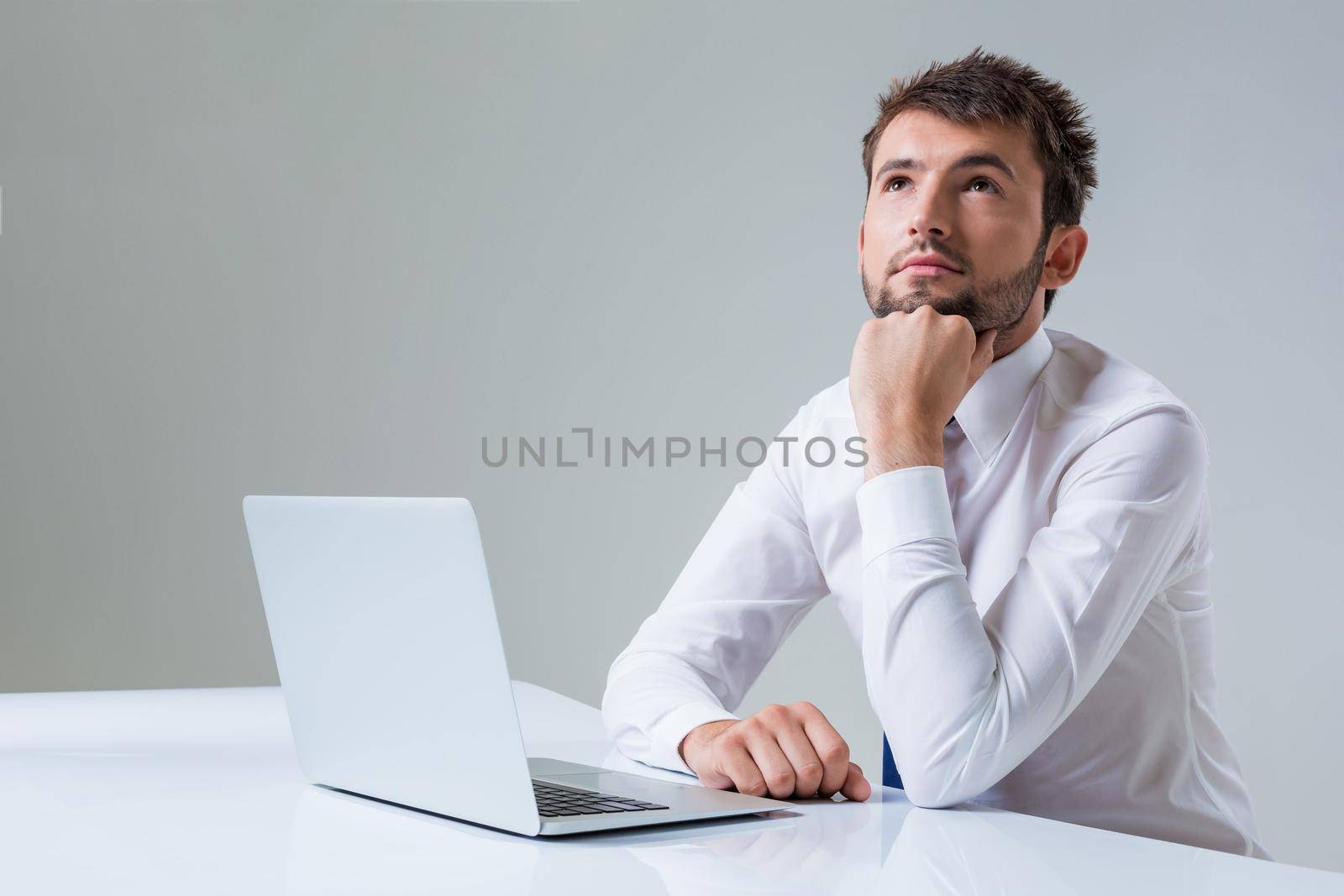 young man thinking uses a laptop computer while sitting at a table. Office clothing