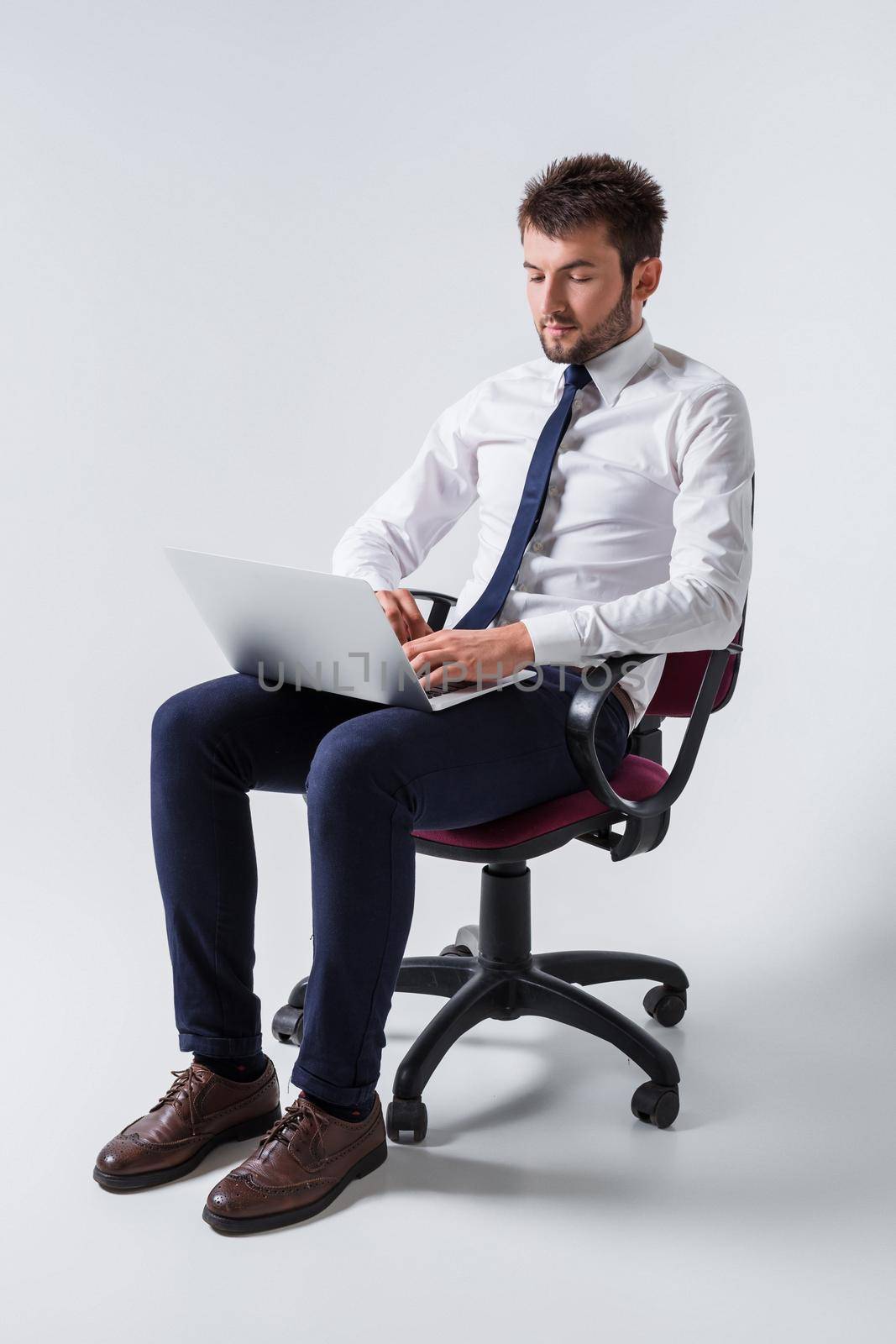 emotional young guy in office clothes working on a laptop computer and sitting on a chair