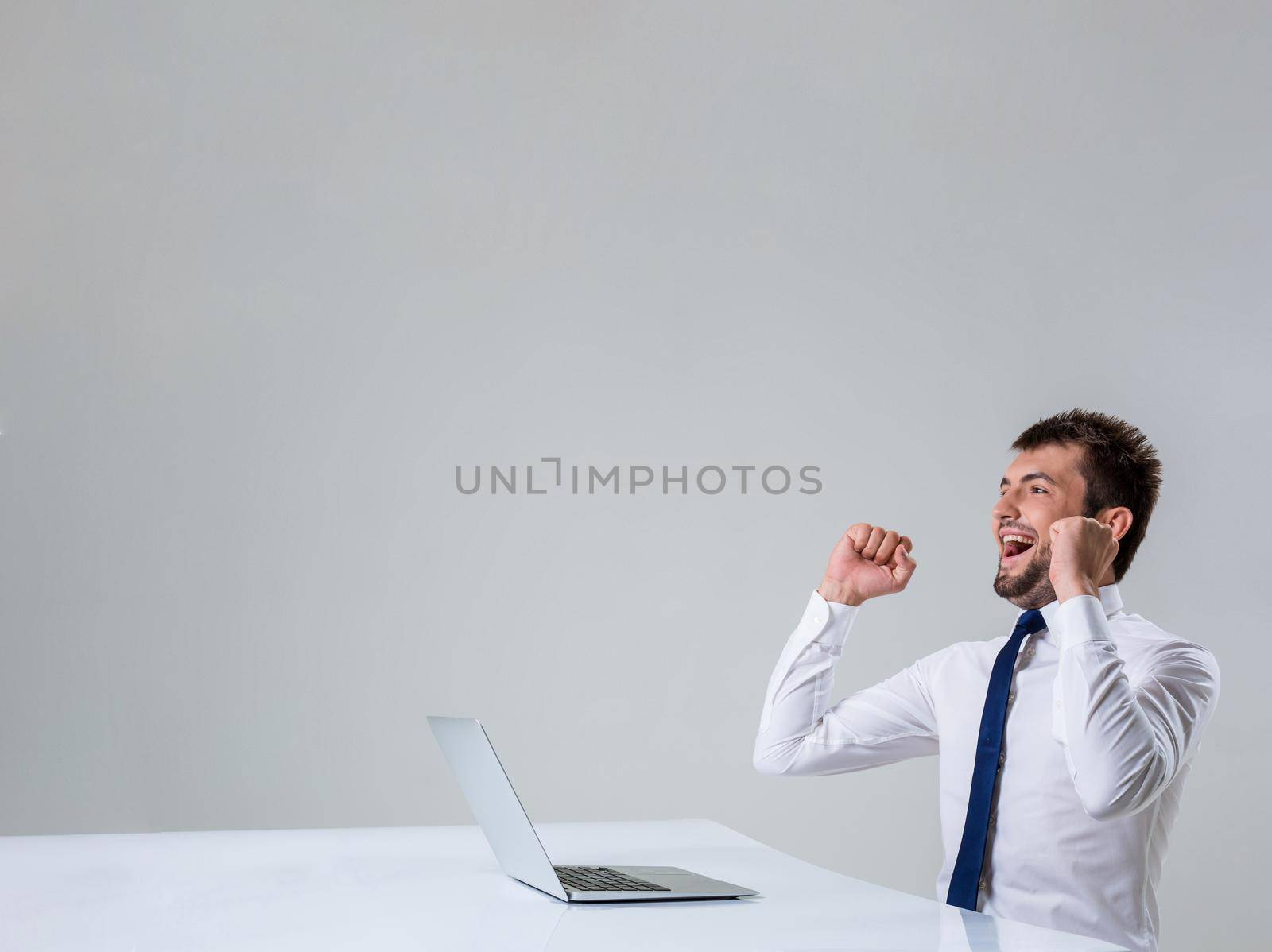 the young man behind the laptop. It uses a computer while sitting at a table. enjoys hands up. Office clothing. Copyspace