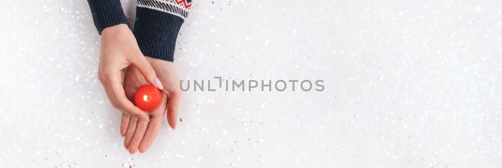 Female hands in sweater holding red candle with flame. Winter holiday, Christmas, Valentine's day background. Giving warm and love concept. Xmas backdrop for web design or postcards. New's Year banner