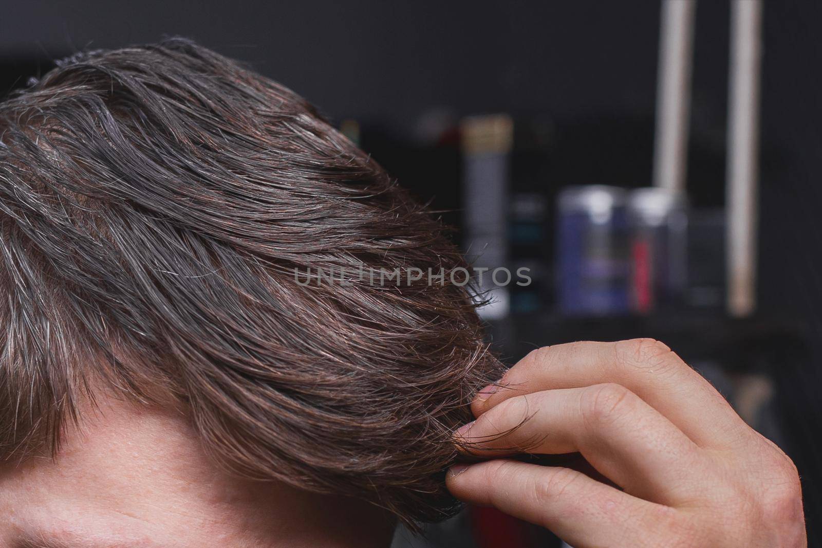 A man's hand touches his dark long hair necessary for a haircut and in need of hairdressing services.