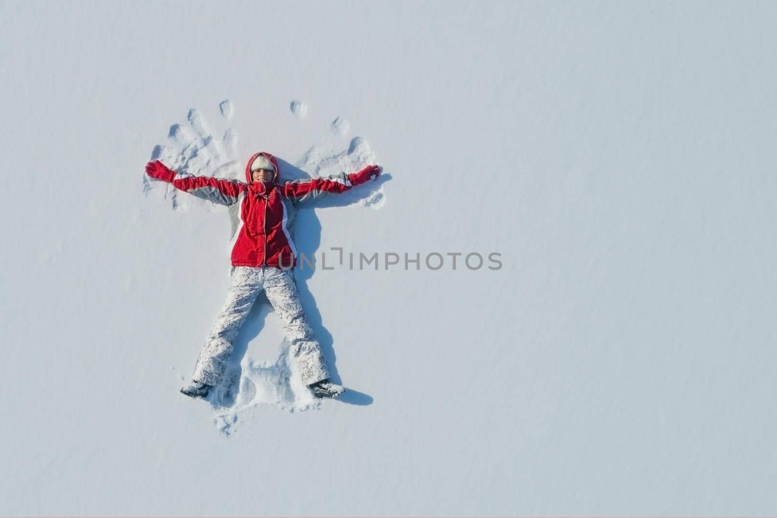 Top view of young girl is lying on the snow and making angel wings. Copy space.