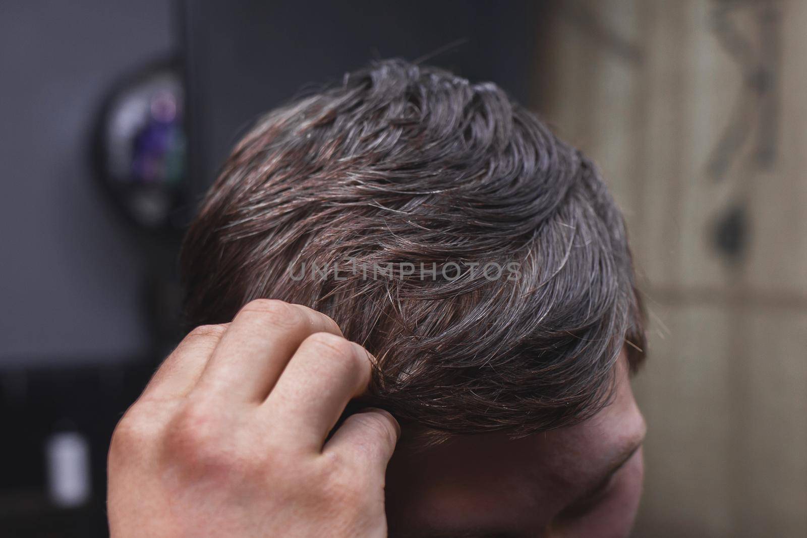 A man's hand touches his dark long hair necessary for a haircut and in need of hairdressing services.