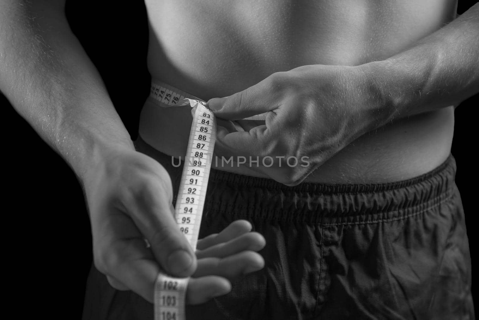 Unrecognizable man is measuring waist, monochrome image