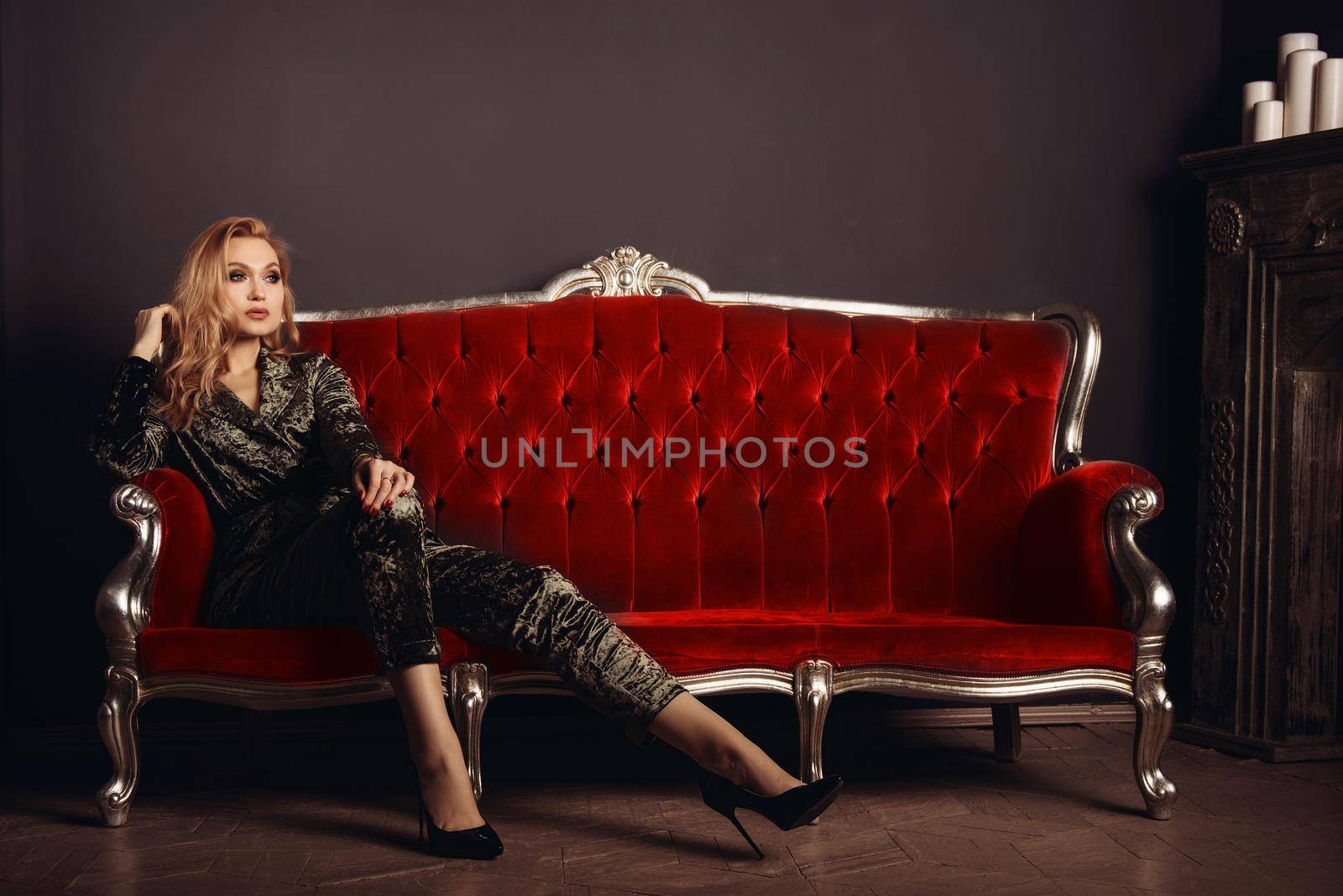 Beautiful young woman in a velor suit sits on a red vintage couch.