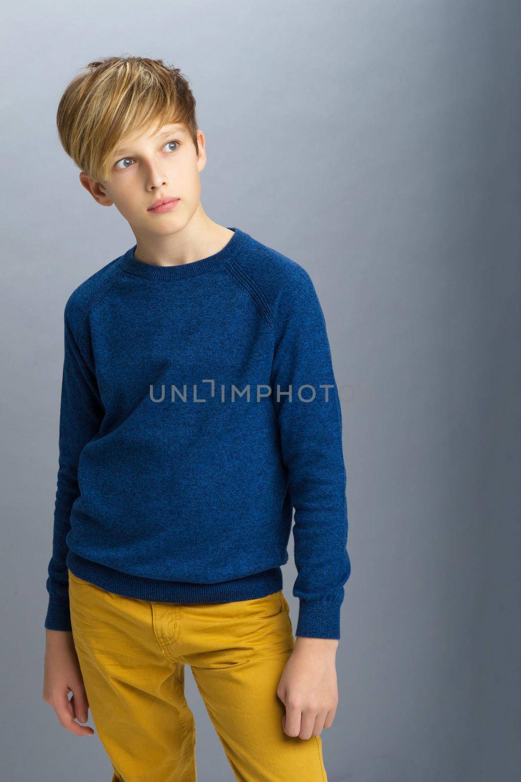 Portrait of stylish teenage boy. Handsome teenager wearing blue pullover and yellow pants posing in studio. Shot of student teenager with serious face expression
