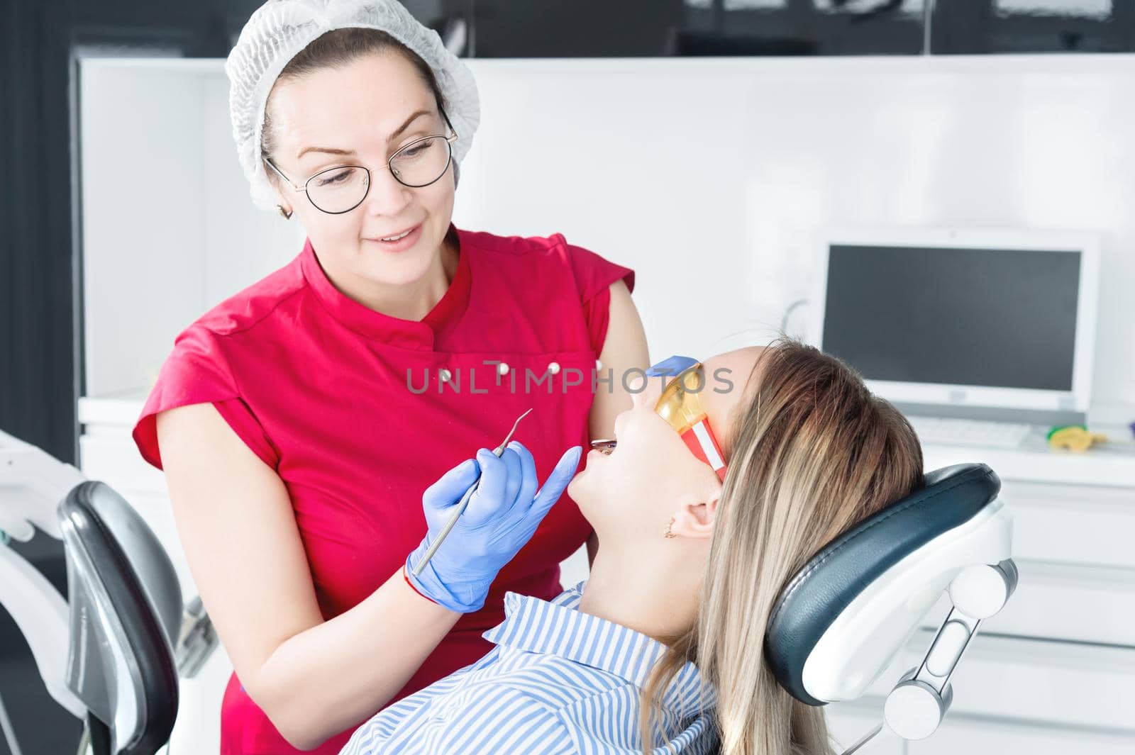 In the dentist's office. A female positive dentist in glasses is preparing to make a cast of the jaw of a young girl patient. Care clean mouth.