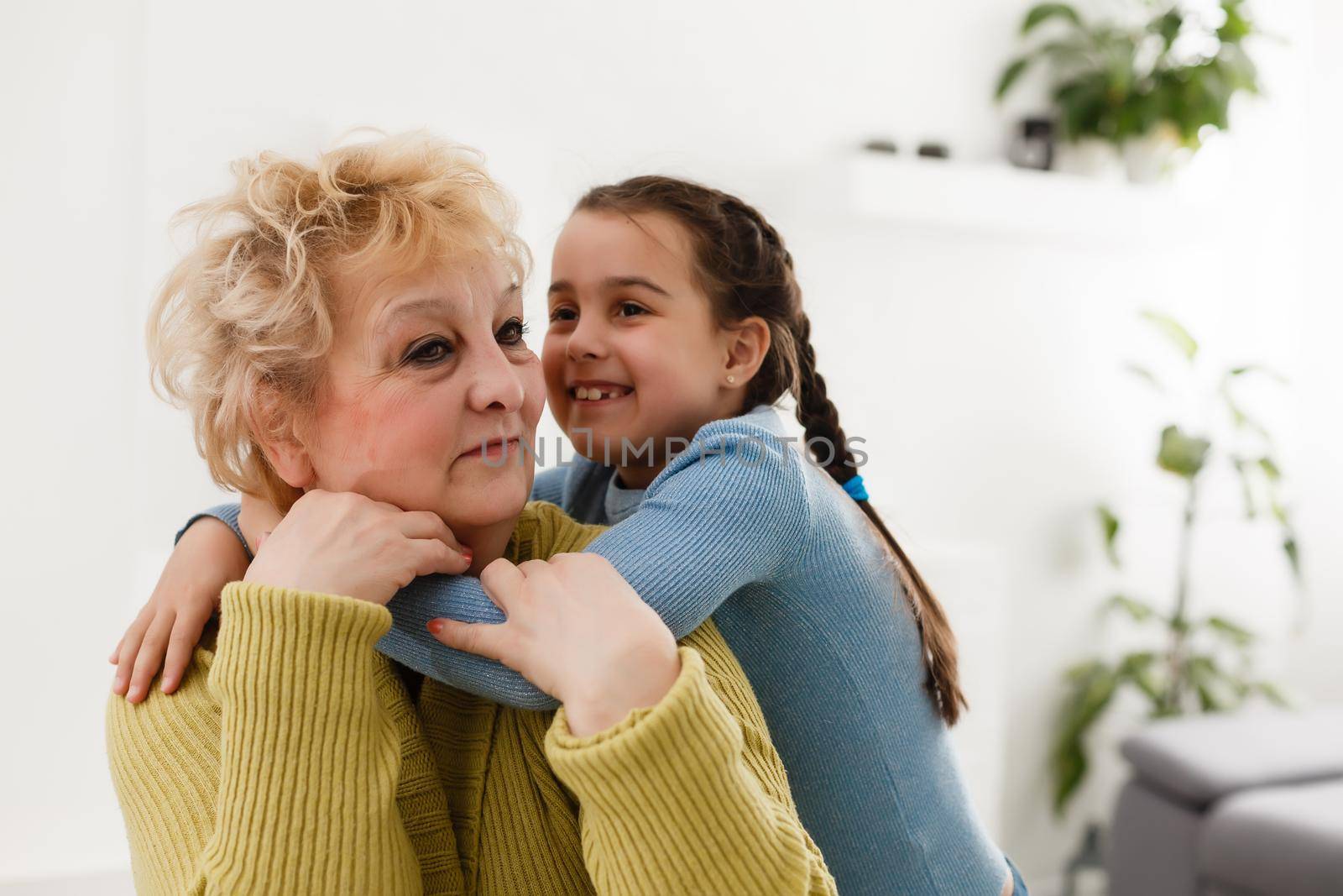 Senior woman hugging granddaughter while sitting on sofa at home
