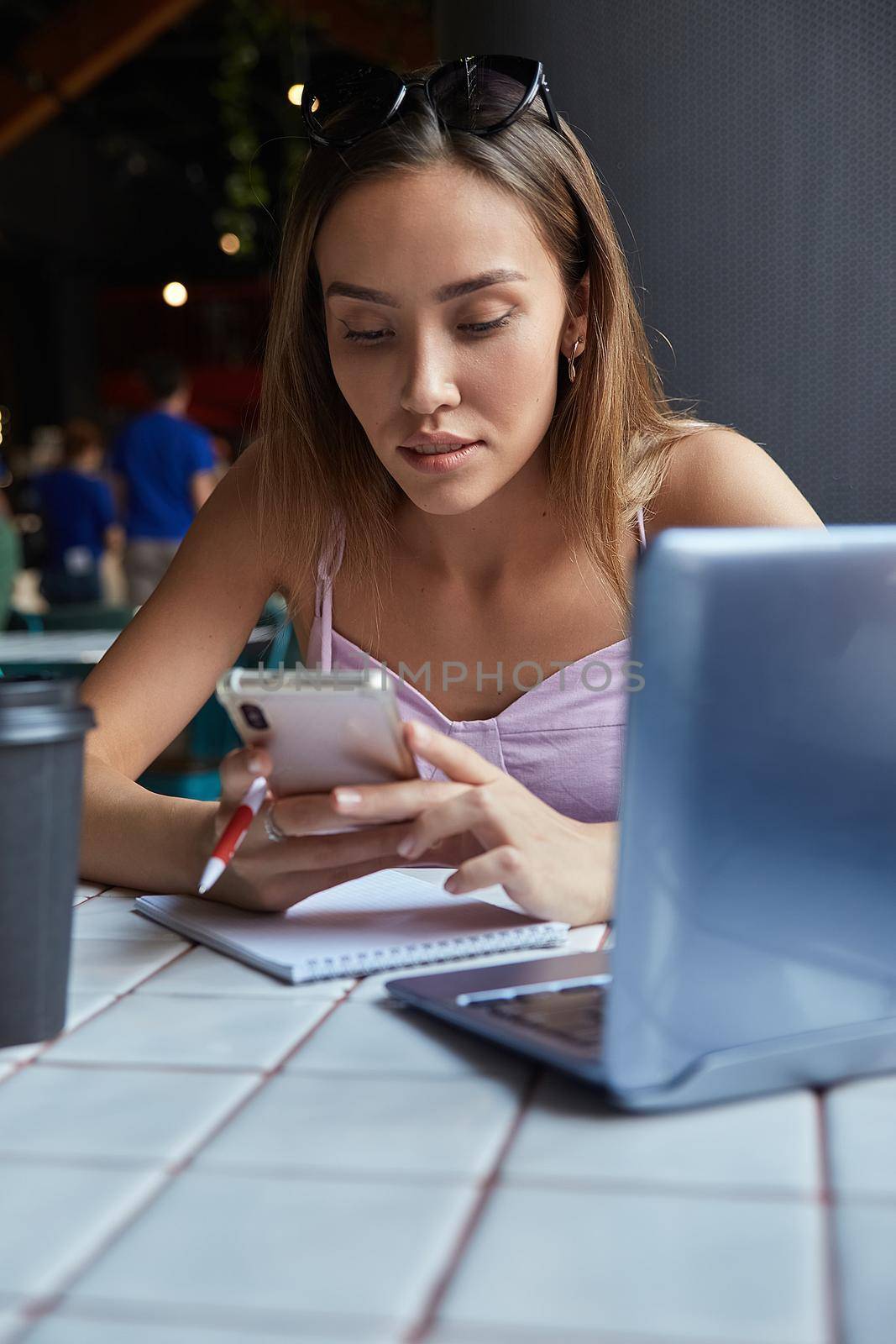 young well dressed asian woman sitting at table, using her smartphone. beautiful lady surfing internet on cell phone at cafe, chatting online. modern communication technology, distant work, remote job