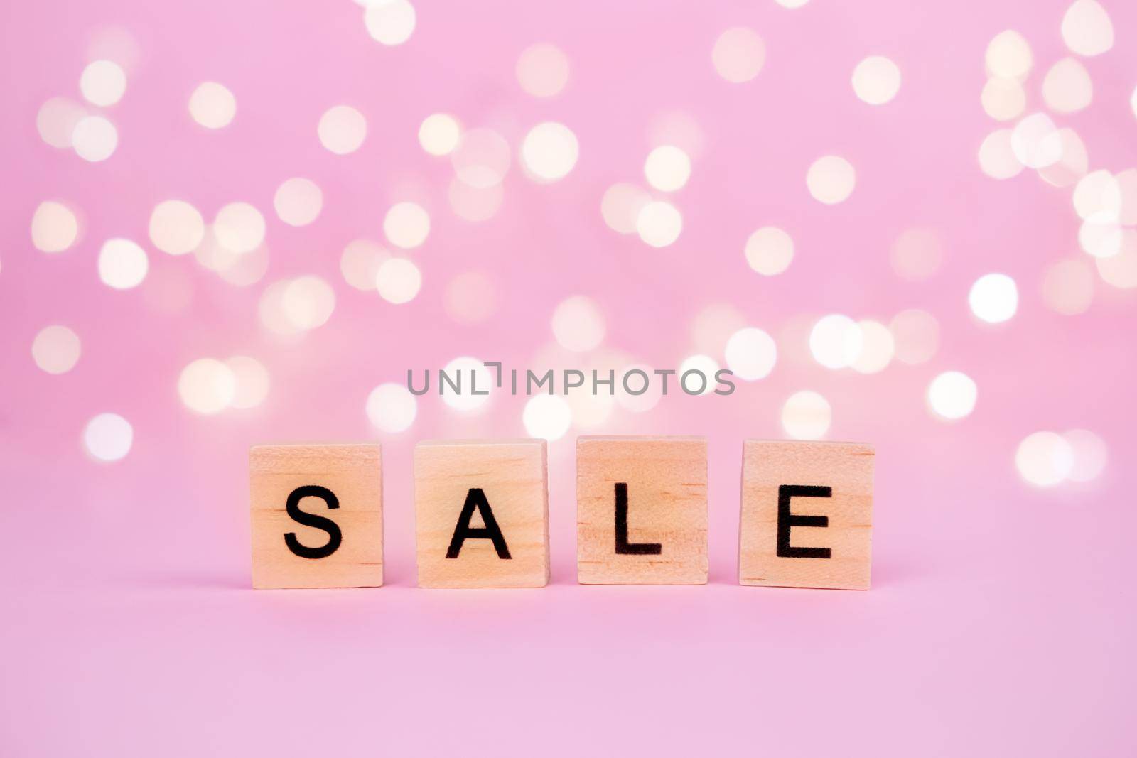 Words Sale on a blurred pink background with beautiful bokeh garland lights. With copyspace Concept of holidays christmas, valentine's day, black friday, mothers day and seasonal discounts