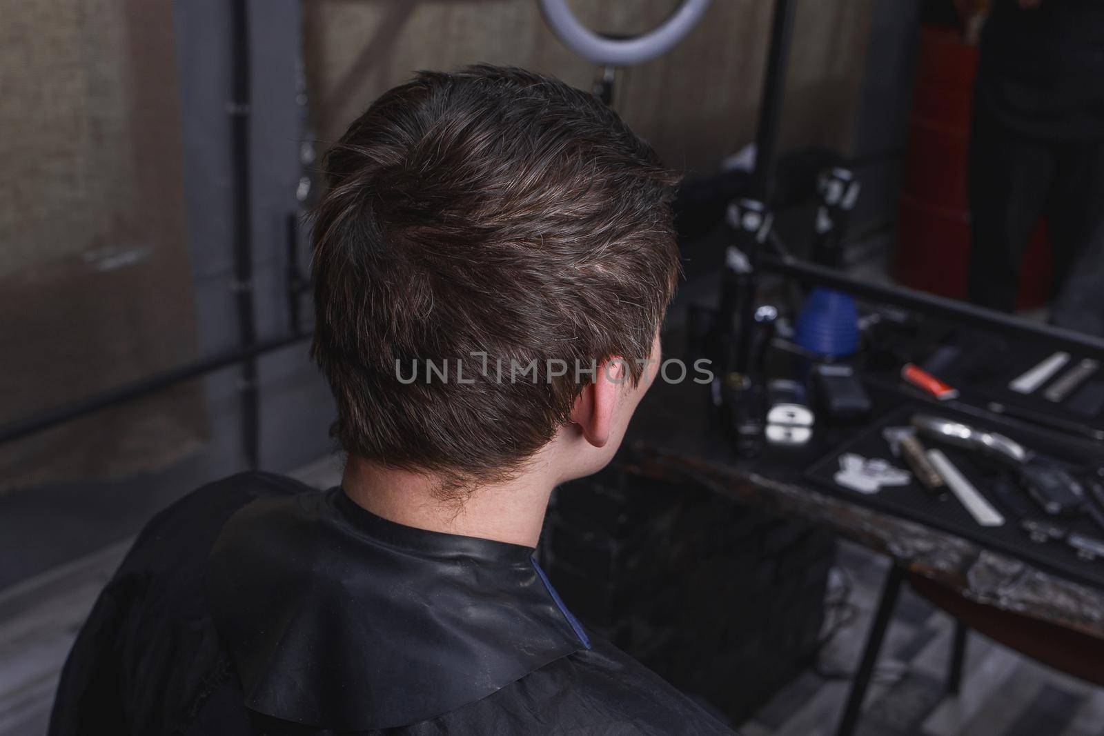 An untrirned guy with dark hair sits on a chair in a salon in front of services and a haircut in a barbershop.