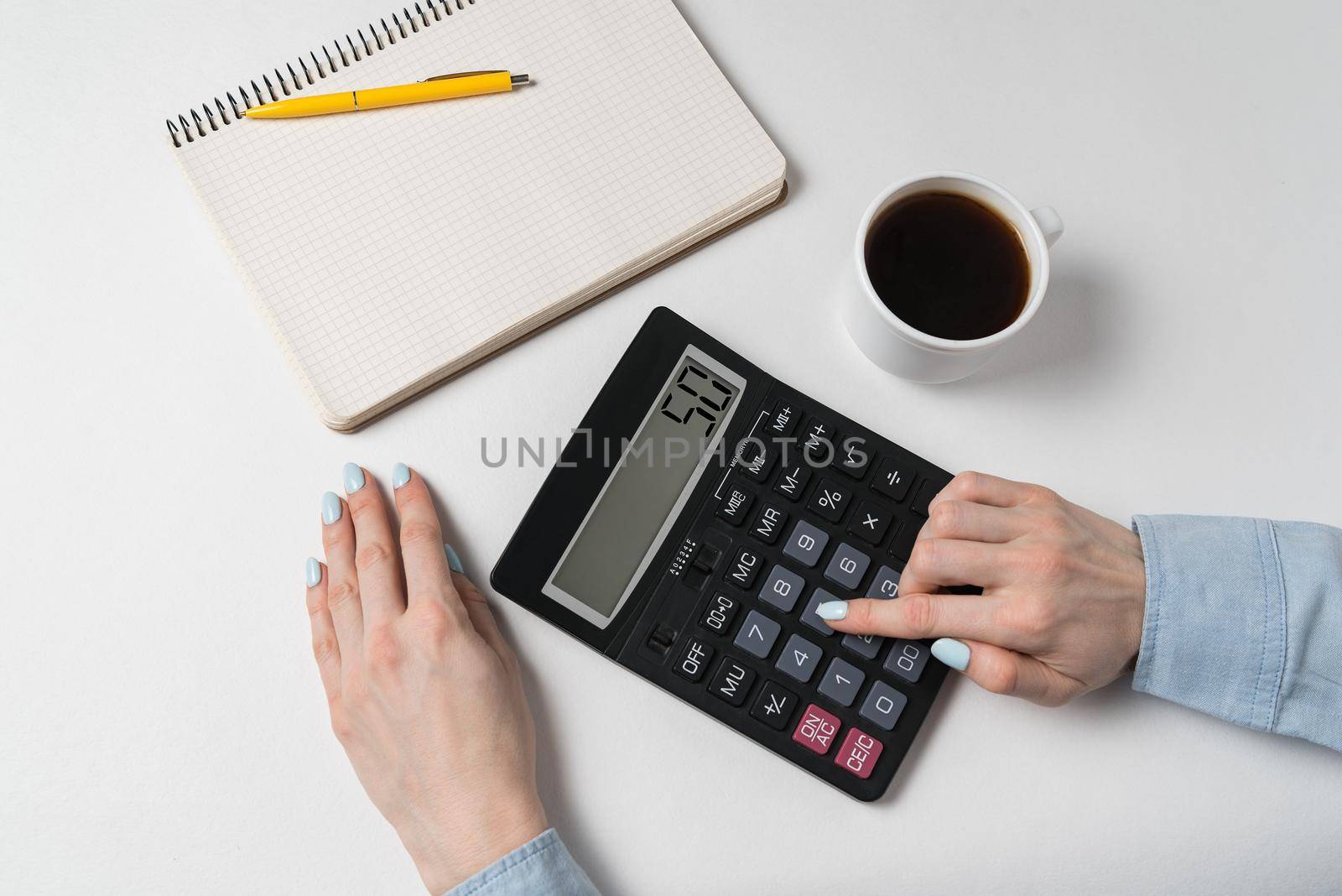 Hand of young woman using calculator. Budget planning concept. White background, top view.