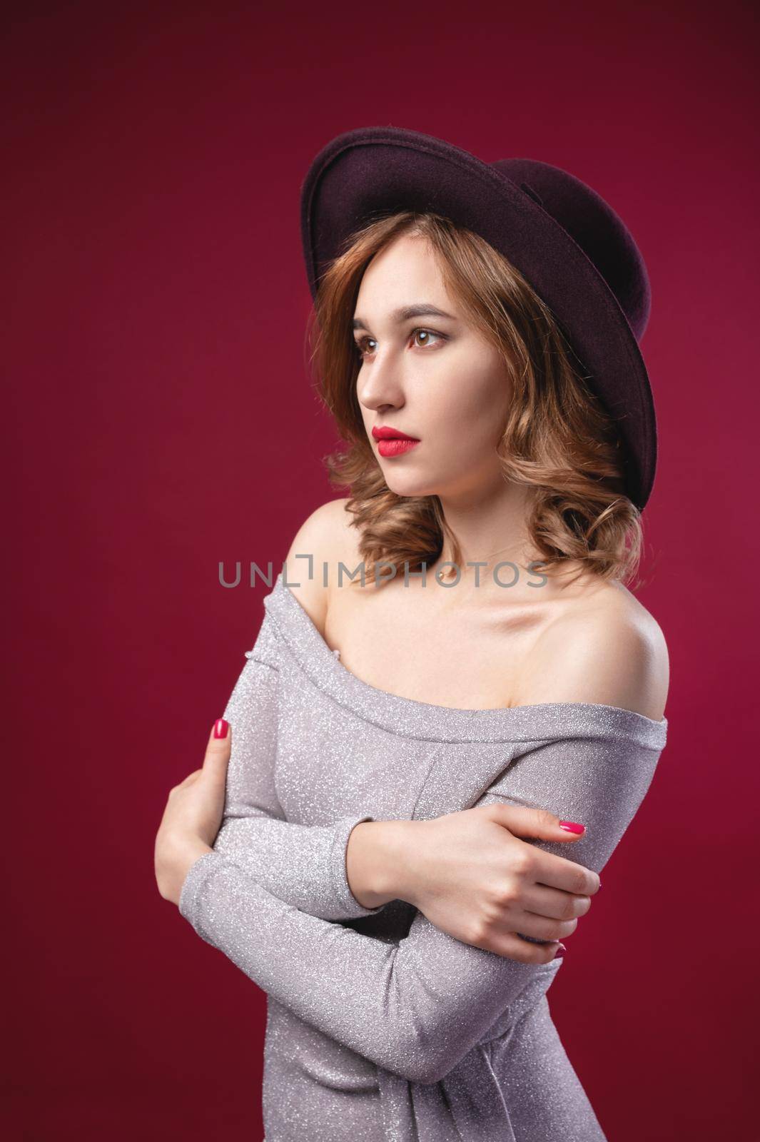 Fashionable attractive Caucasian girl in a large hat to large brim in a silver shiny dress on a red background. Studio retro portrait by yanik88