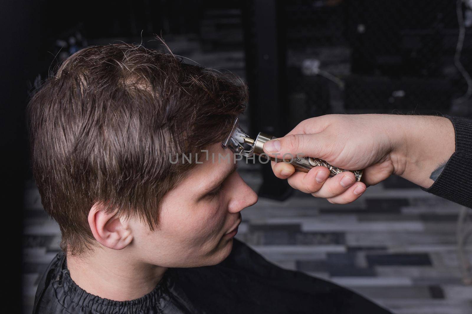 The hand of a barber or hairdresser with a portable clipper cuts the client's man with dark long hair. Hairdressing.