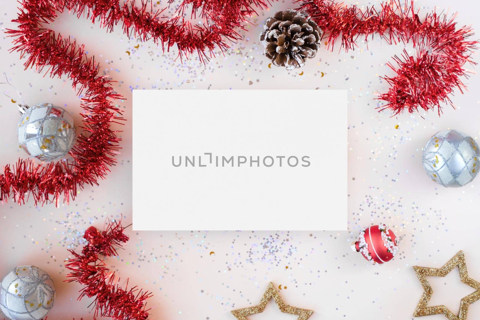 Flat lay xmas composition with isolated white paper. Red tinsel, golden stars, silver Christmas balls, glitter with bokeh lights. New Year backplate for your design or postcard. Happy holidays concept