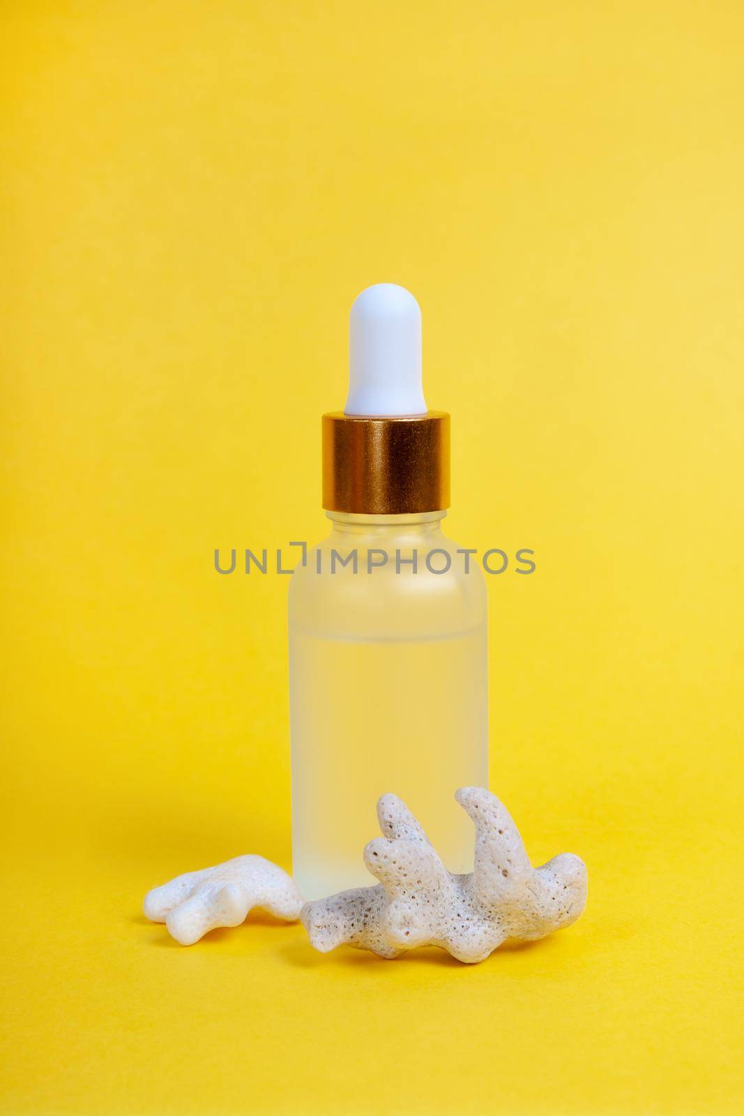 Face care in a glass dropper bottle with sea coral on a yellow background. Skin care concept. Vertical photography
