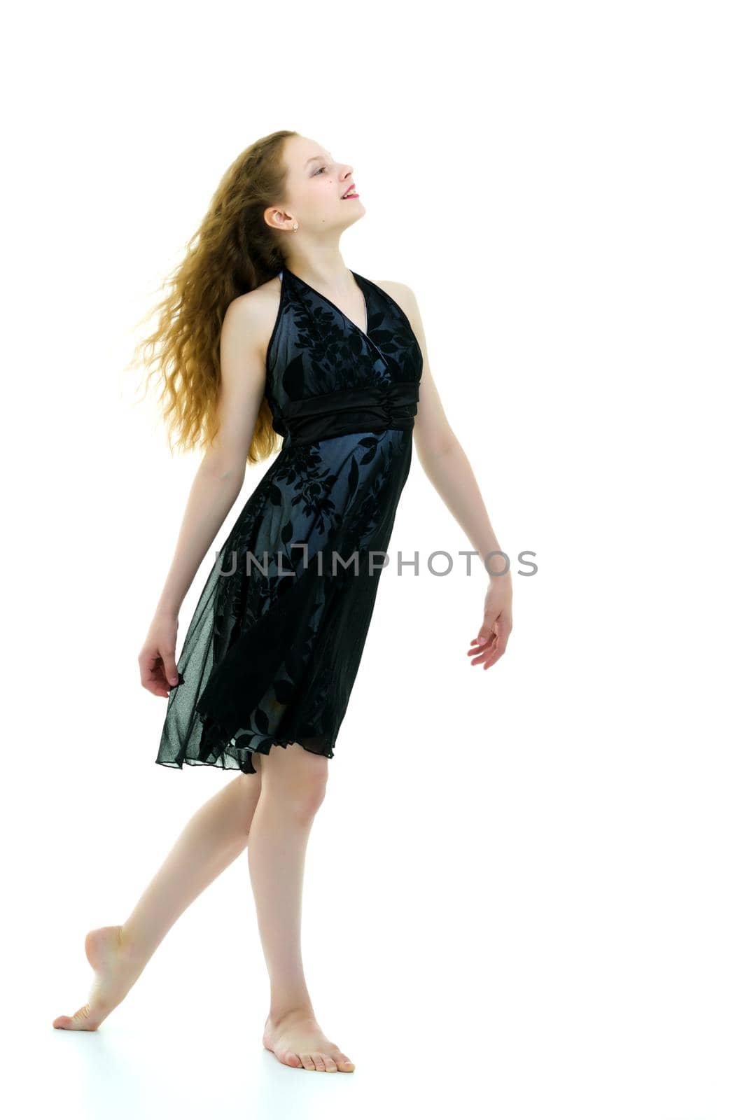 Portrait of a positive and stylish little girl in a summer dress, rejoices in the wind that blows and moves her dress and hair. The concept of beauty and fashion. Isolated on white background.