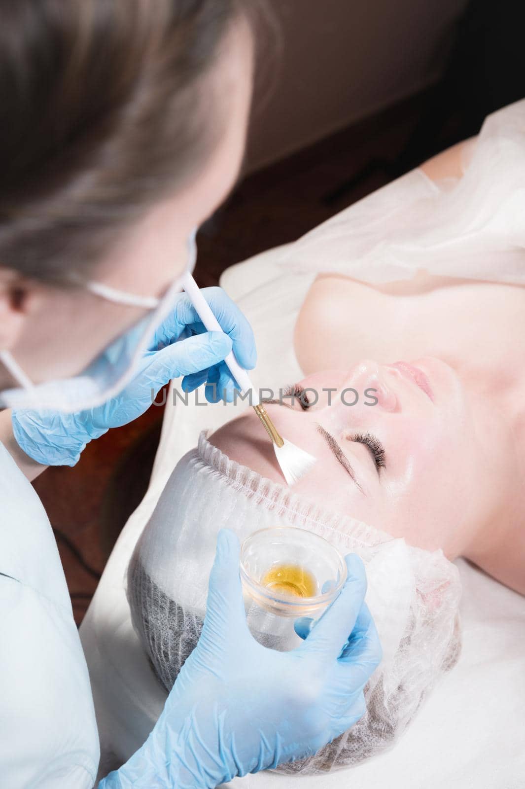 face of a young woman close-up lying down cosmetic procedure is performed applying a rejuvenating mask. by yanik88