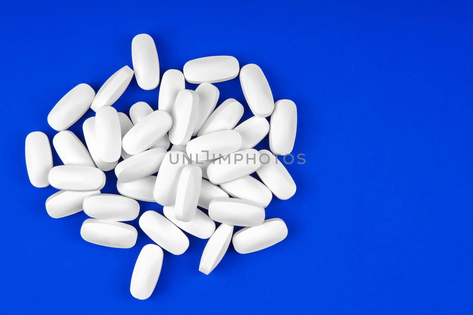 Heap of medical white pills on a blue background top view