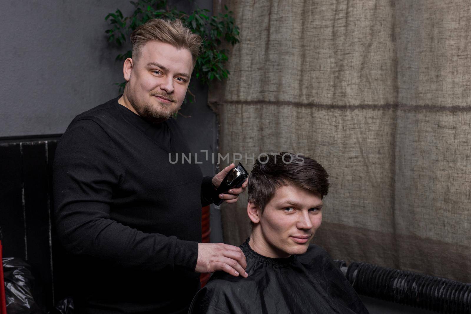 Barber European looking man hairdresser cuts the client with dark hair. Hairdressing.