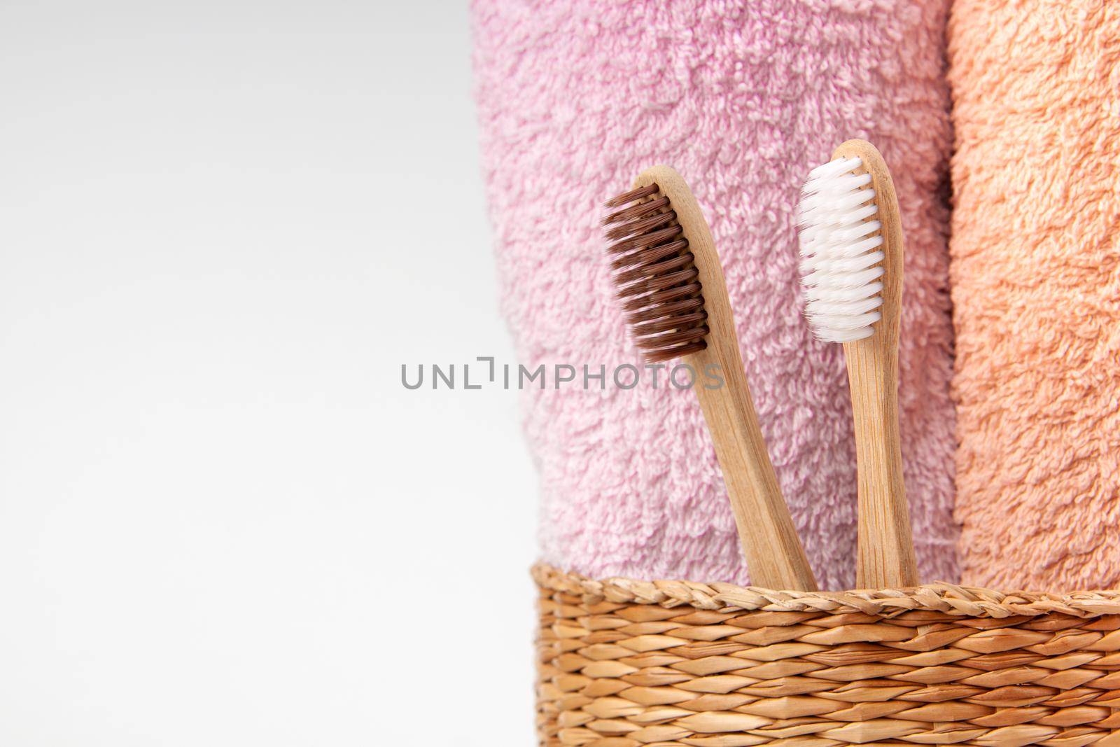 Bamboo toothbrushes with towels in a wicker wooden basket with copy space on white background. Spa, healthy lifestyle and ecology concept.