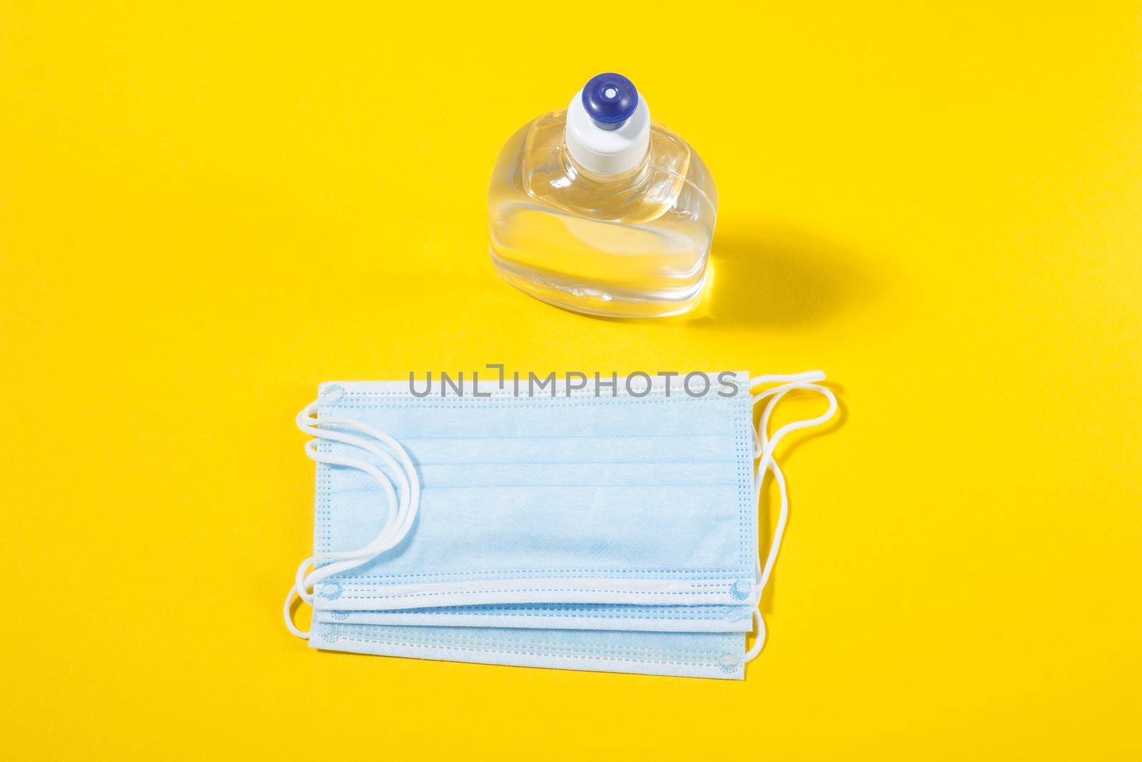 Alcohol gel hand sanitizer and disposable hygienic mask on yellow background